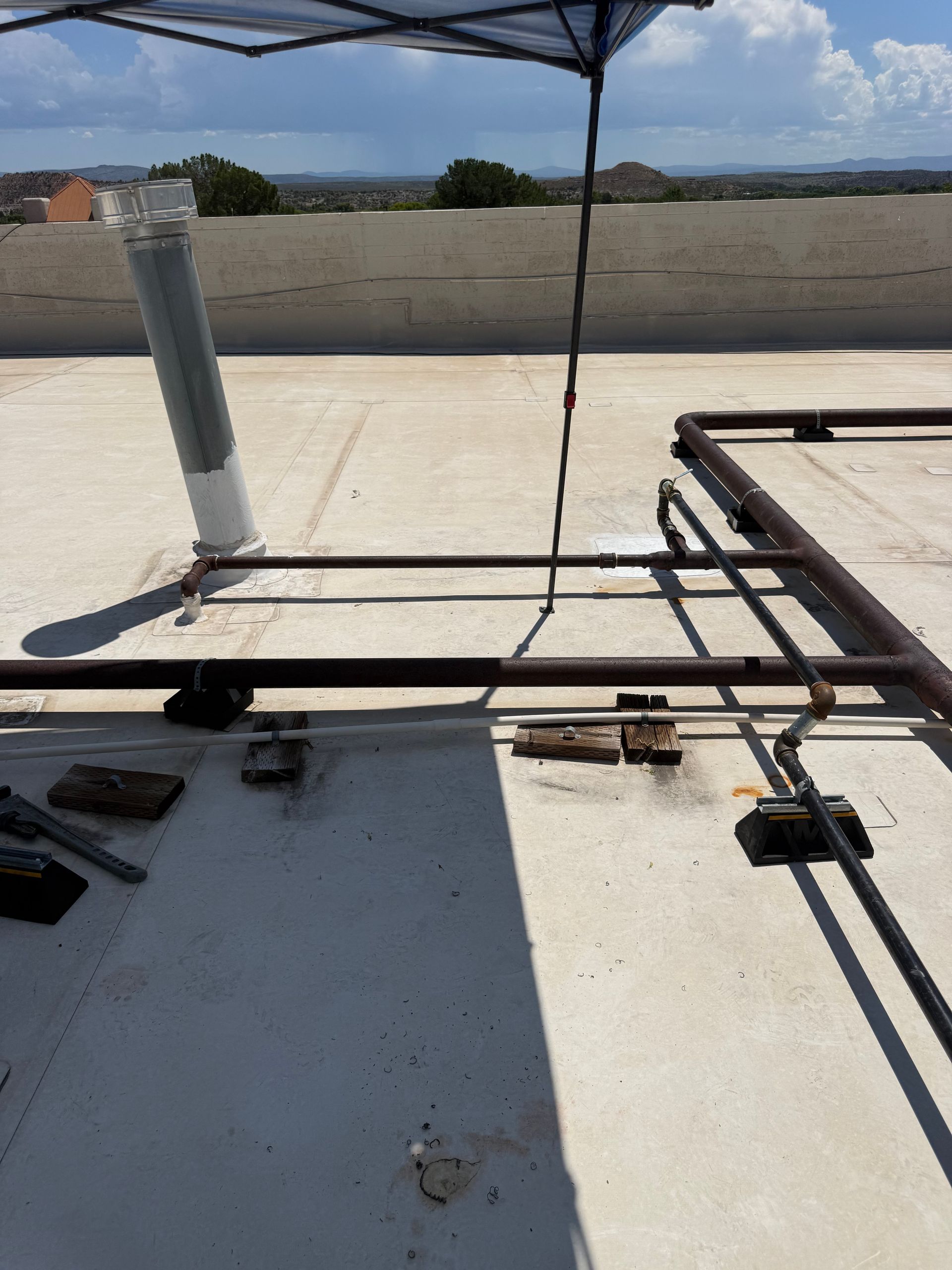 Rooftop with metal rails, pipes, and a canopy frame on a white surface under clear sky.