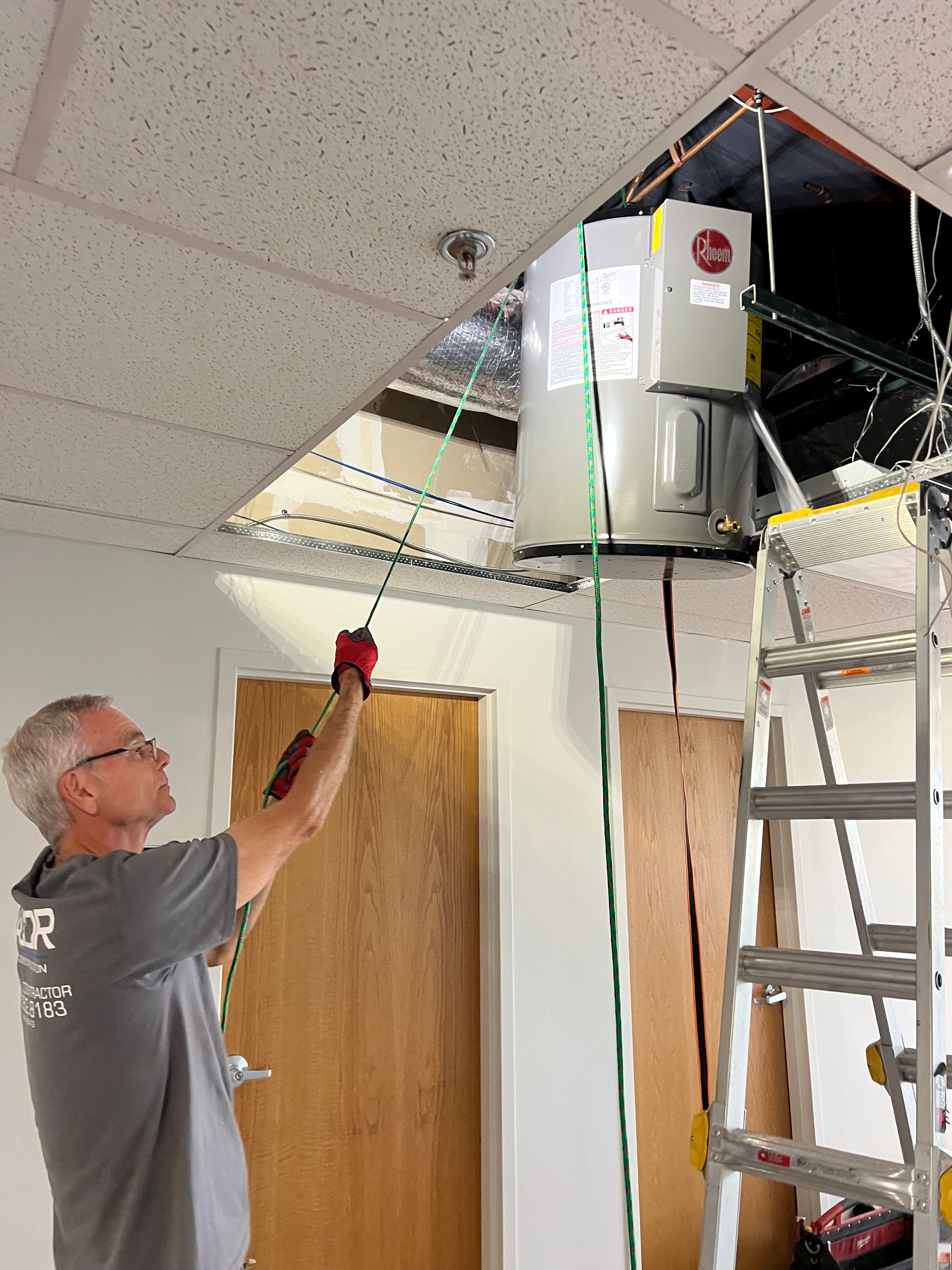 Man installing a ceiling-mounted HVAC unit above a doorway with a ladder nearby.