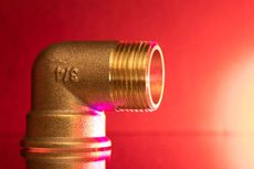 Brass elbow pipe fitting against a red background