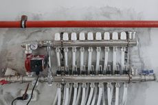 Plumbing manifold with multiple white pipes and valves mounted on a gray wall, with a red pipe above.