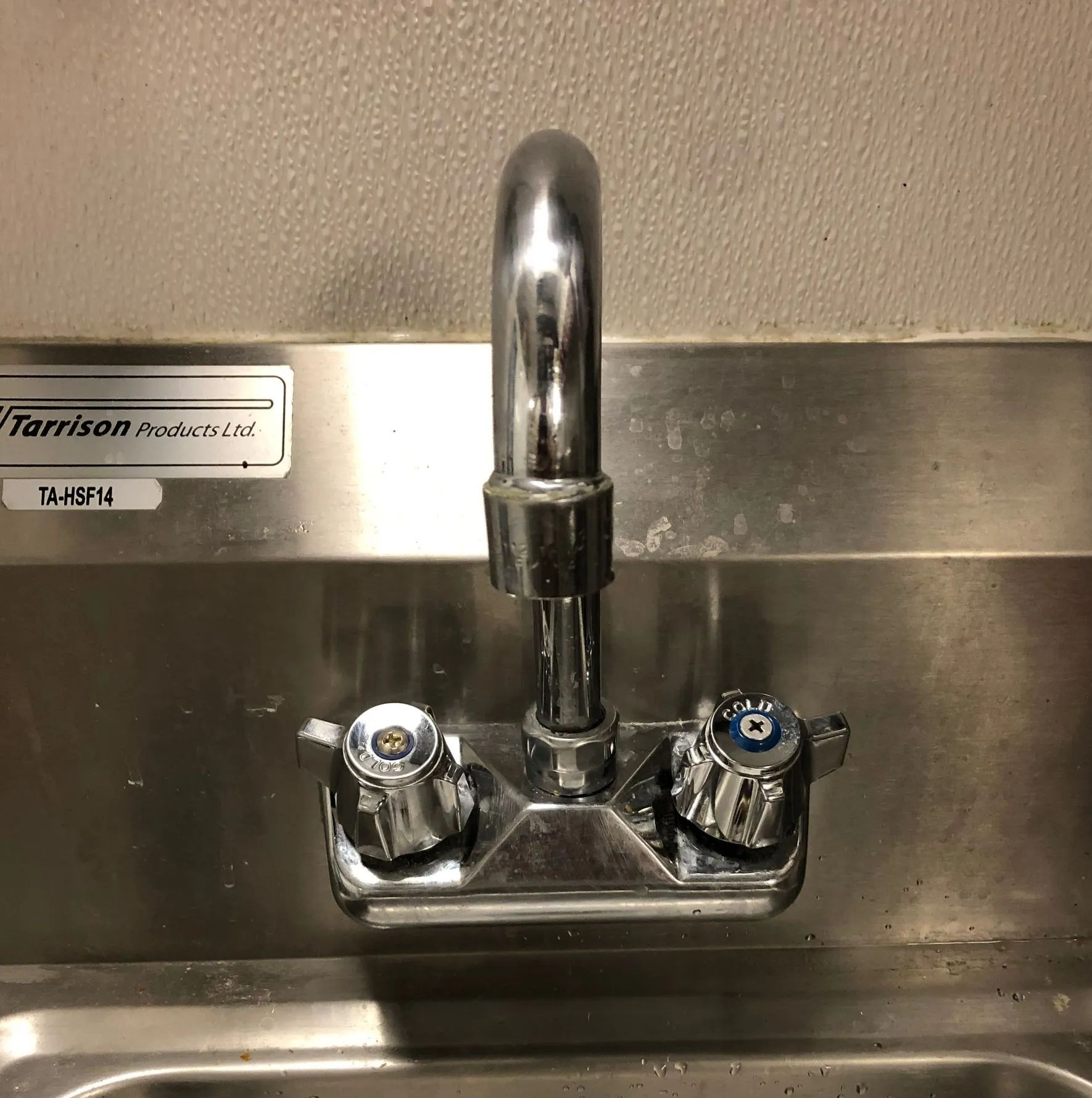 Stainless-steel sink with faucet and two handles on a metal backsplash.