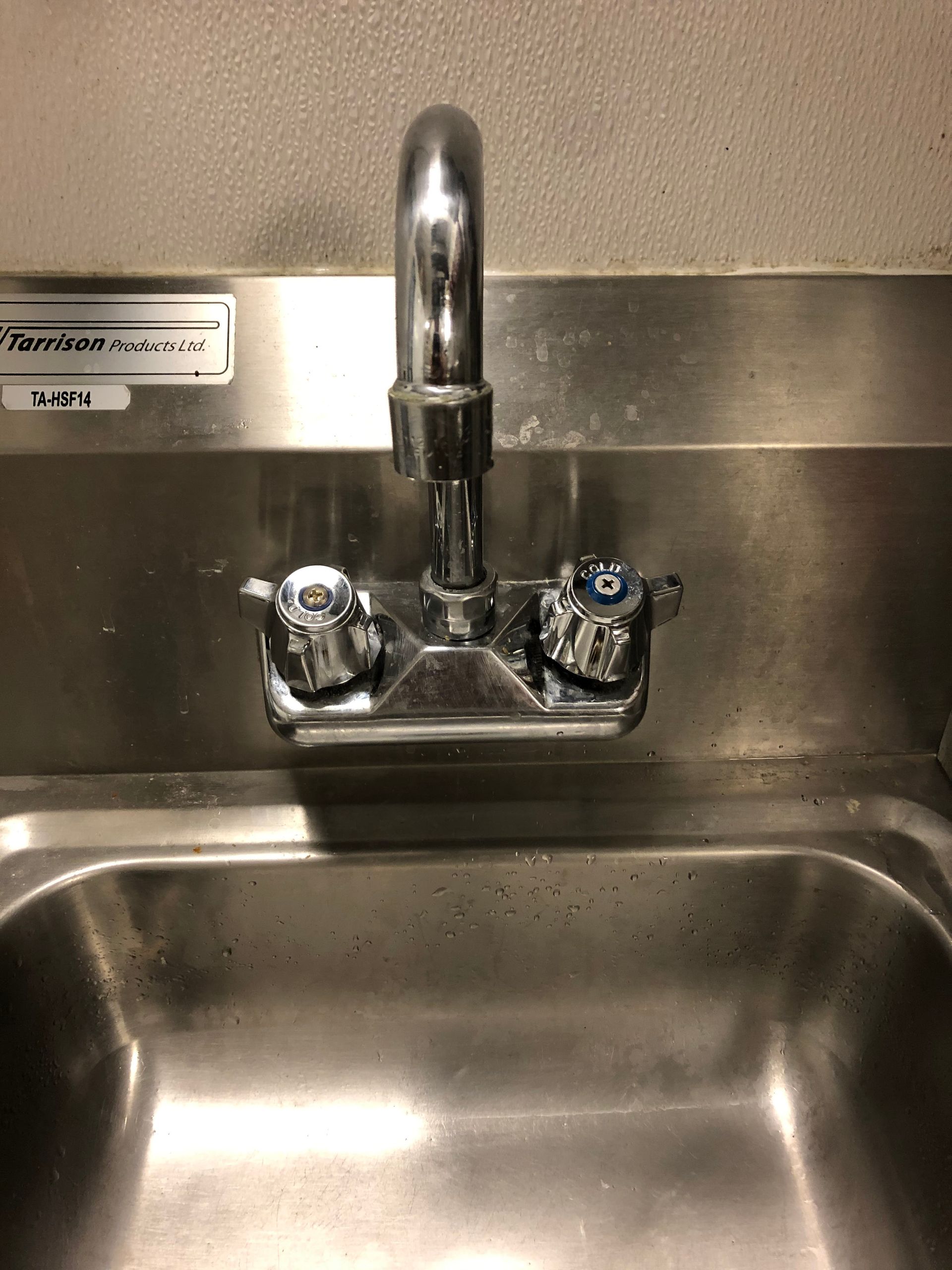 Stainless steel sink with chrome faucet and two handles.