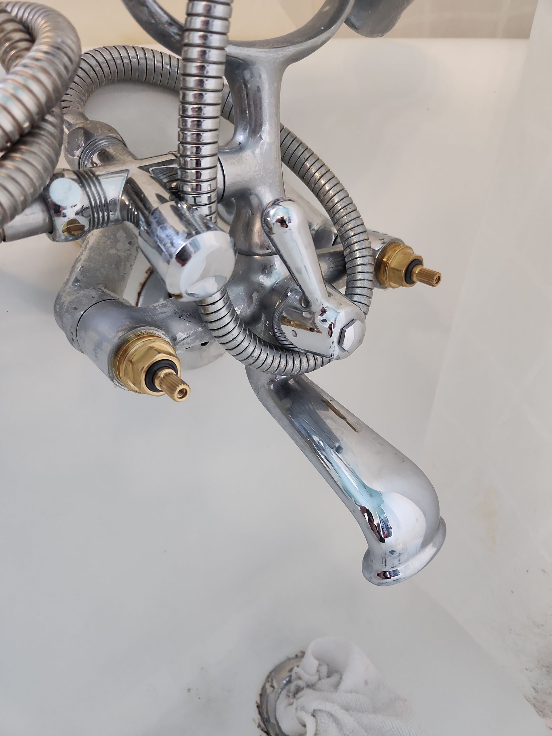Chrome bathtub faucet with attached showerhead hose and brass fittings.