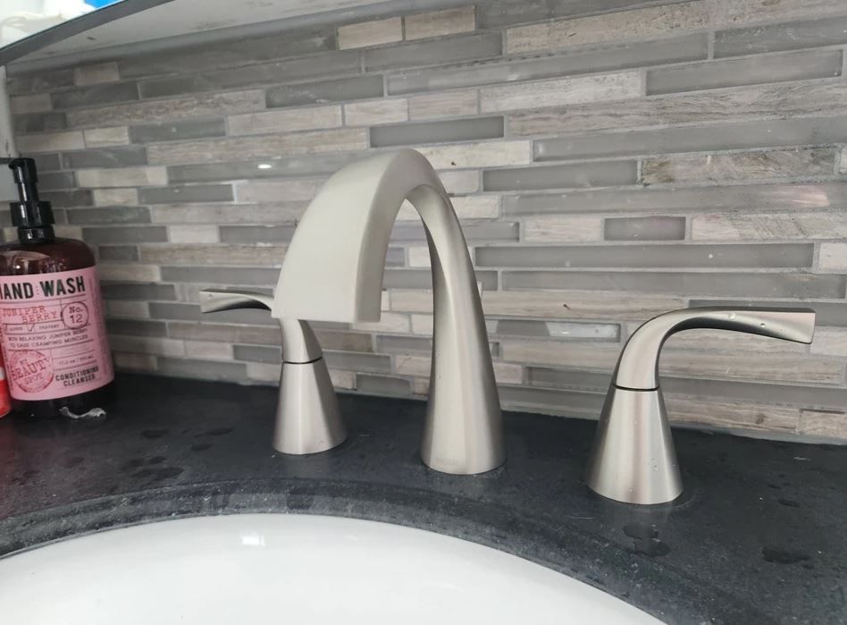 Bathroom sink with a brushed nickel faucet and gray tile backsplash.