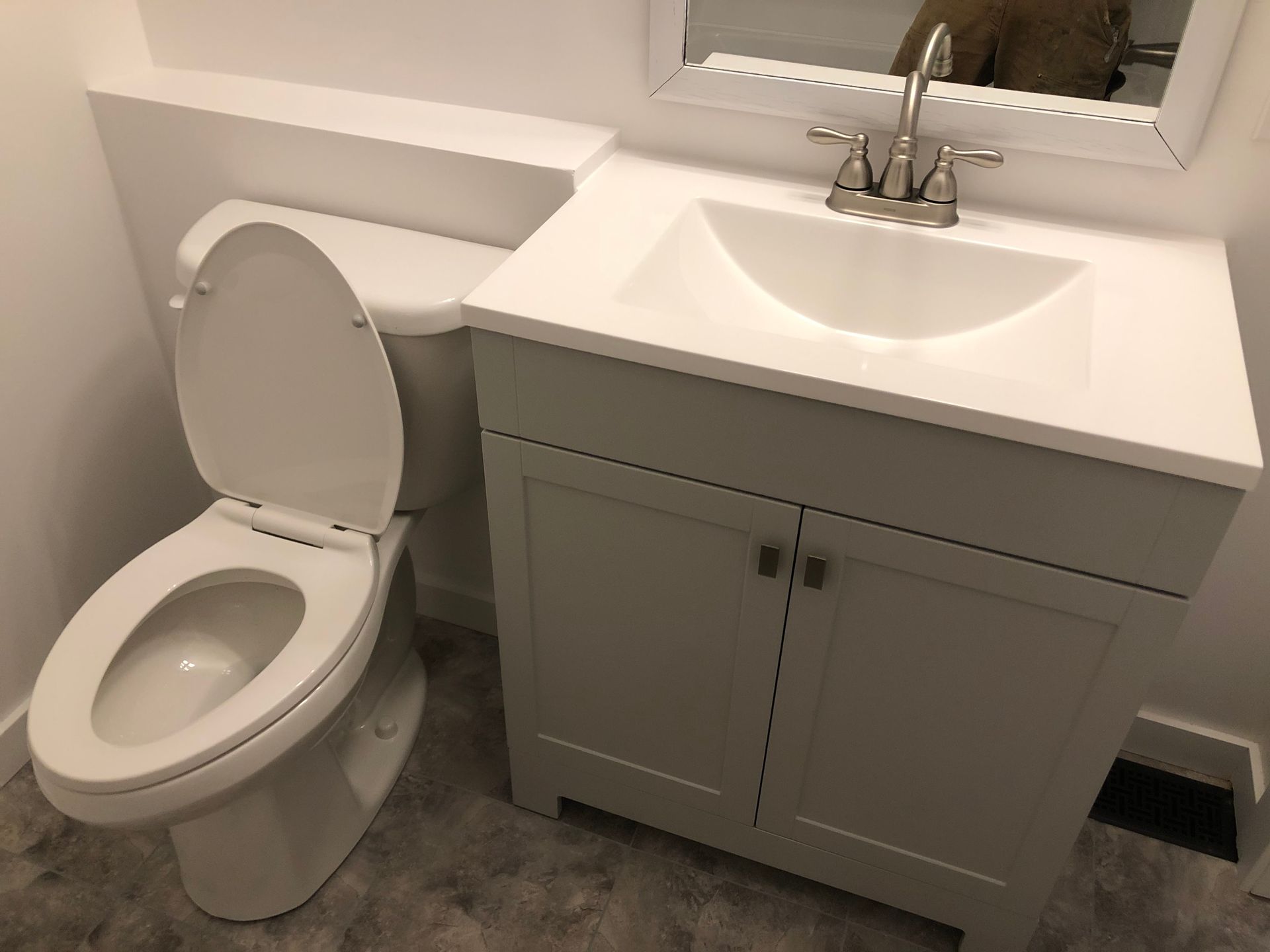 Toilet and white vanity in a bathroom with silver faucet and a mirror.