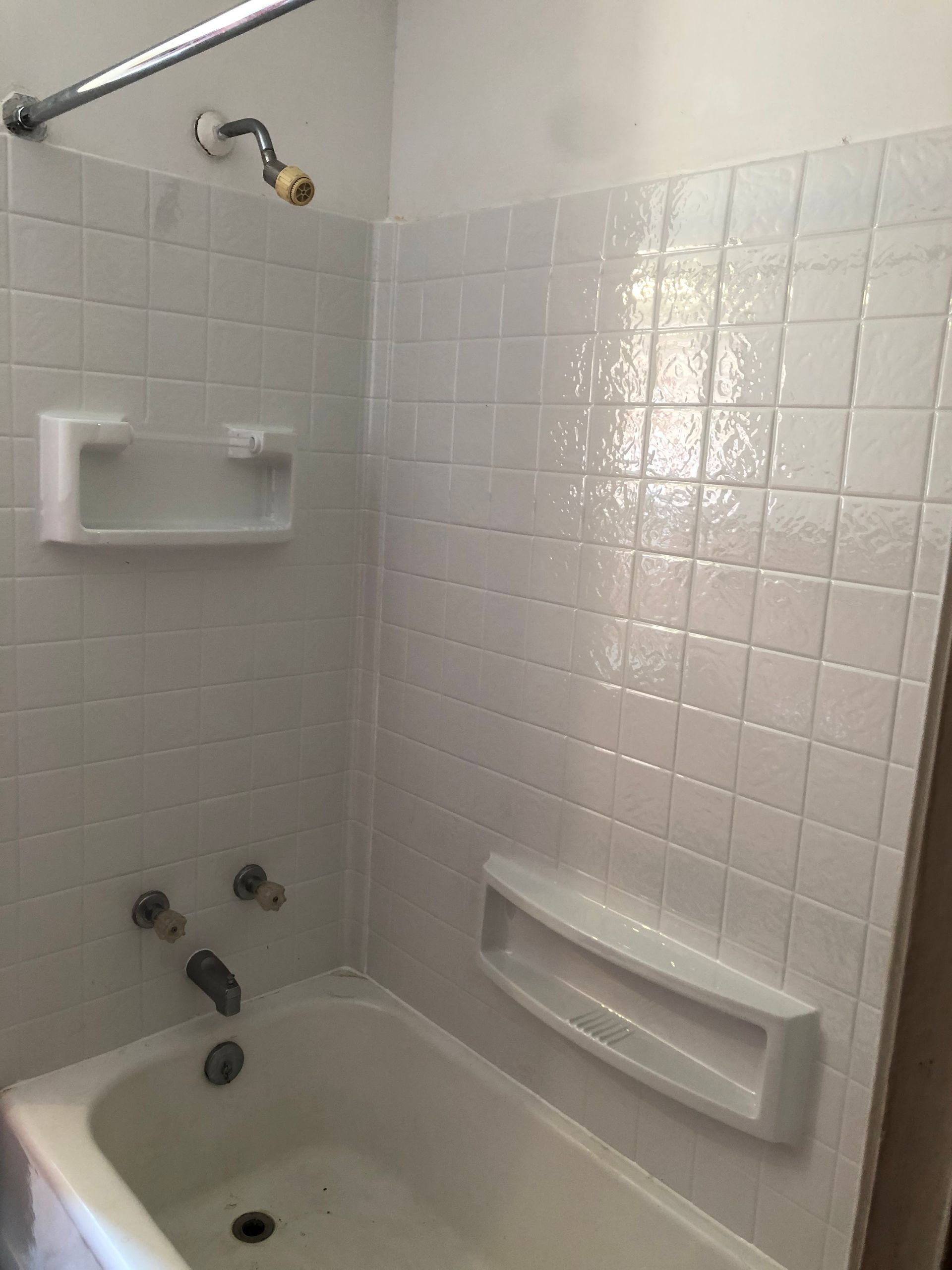 White tiled shower with a bathtub, soap holders, and showerhead.