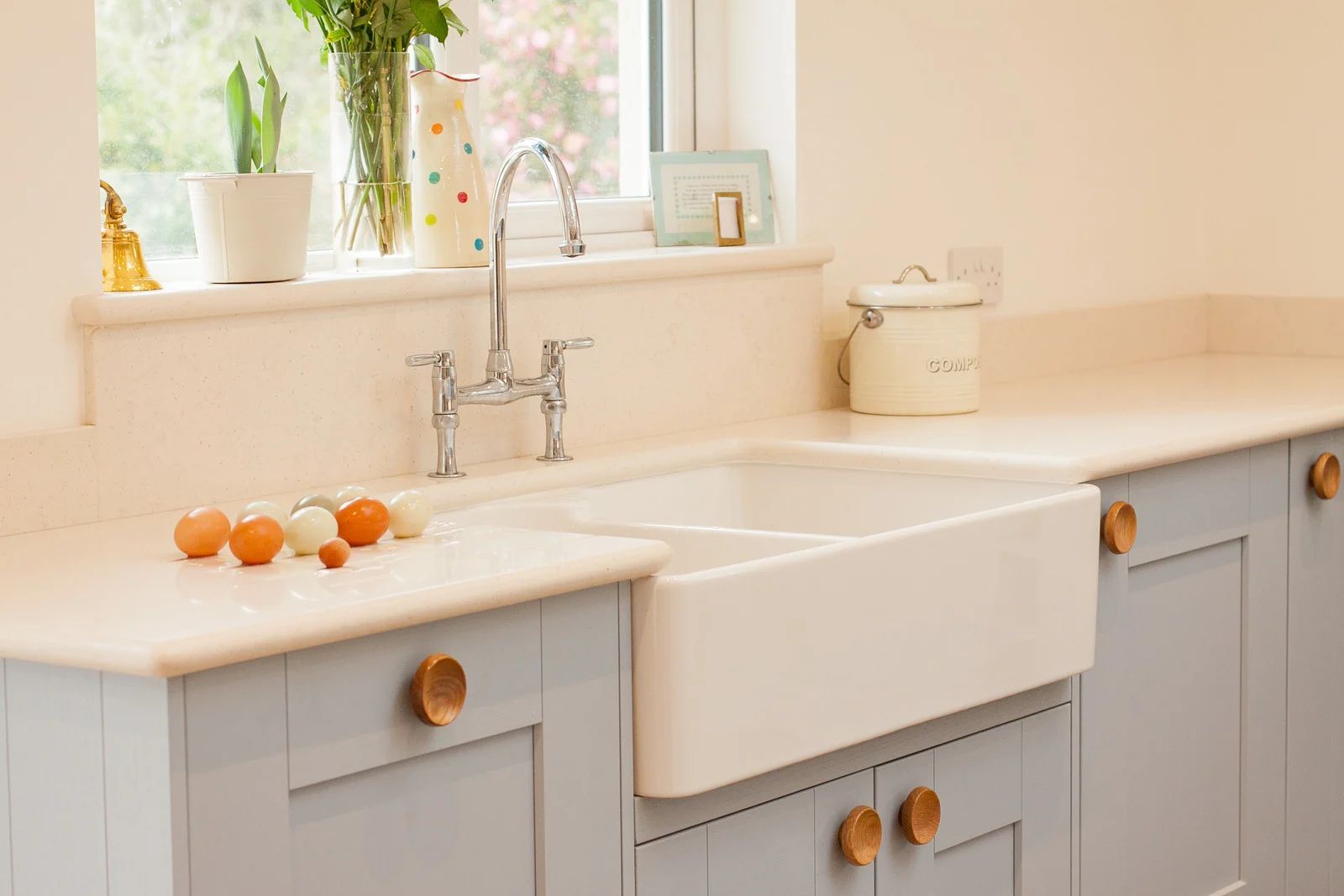 Bright kitchen sink with pale blue cabinets, white countertops, and oranges on the windowsill.