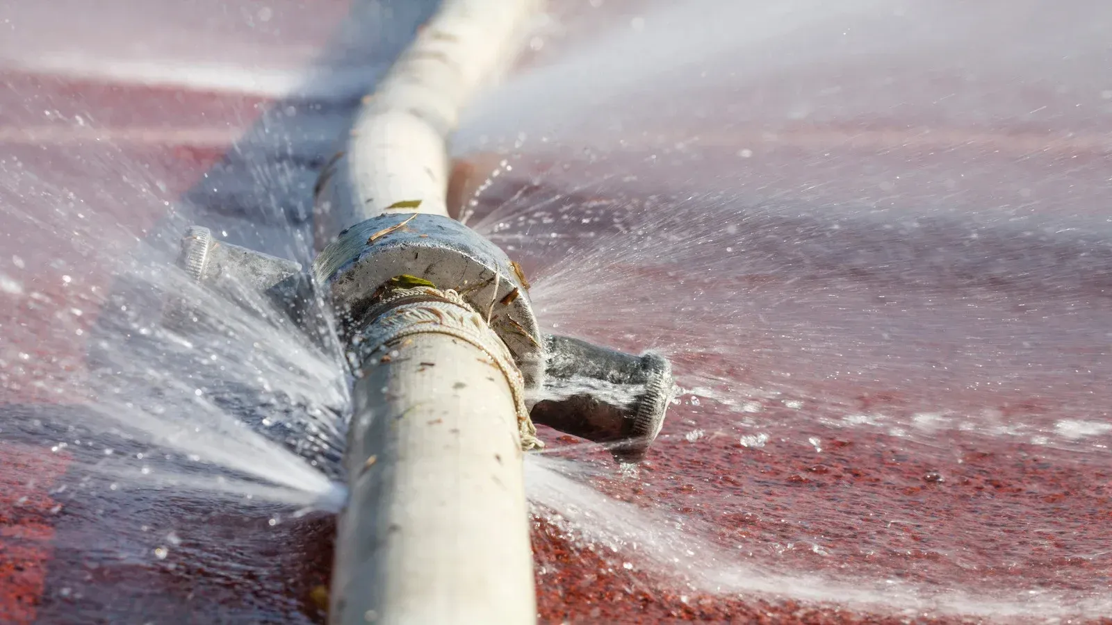 White hose with a leaky valve spraying water on a red surface.