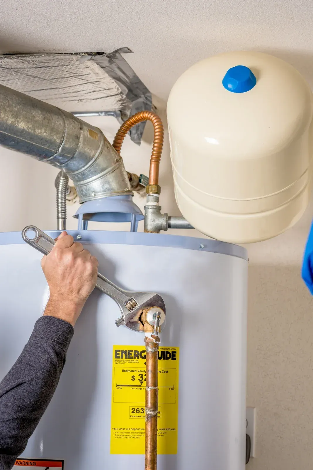 Person using a wrench on a water heater, with an expansion tank nearby.