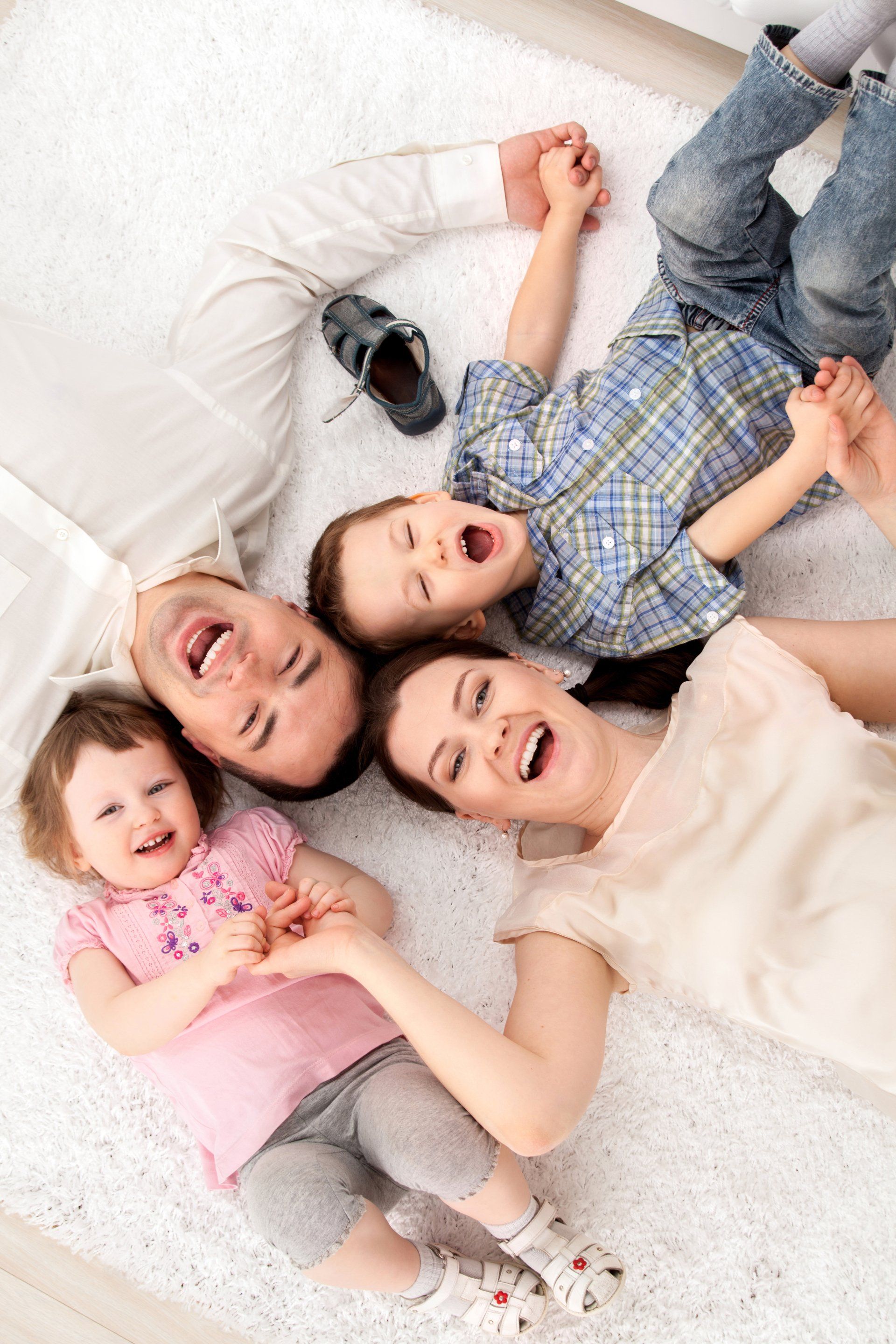 A family is laying on the floor holding hands and smiling.