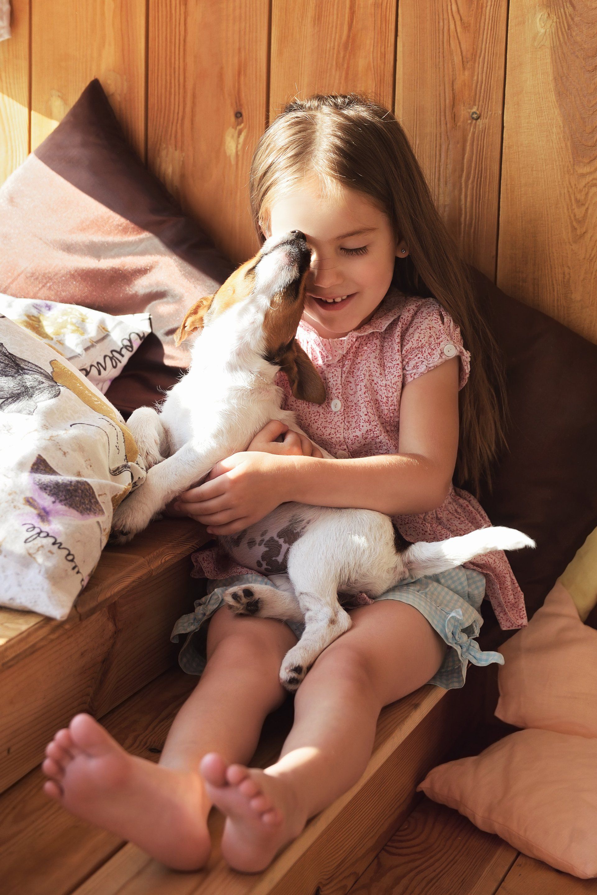 A little girl is sitting on a wooden bench holding a puppy.