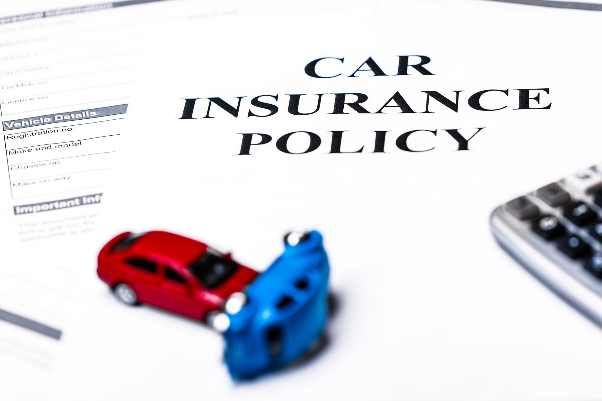 Car insurance policy document with small crash models and calculator representing coverage costs