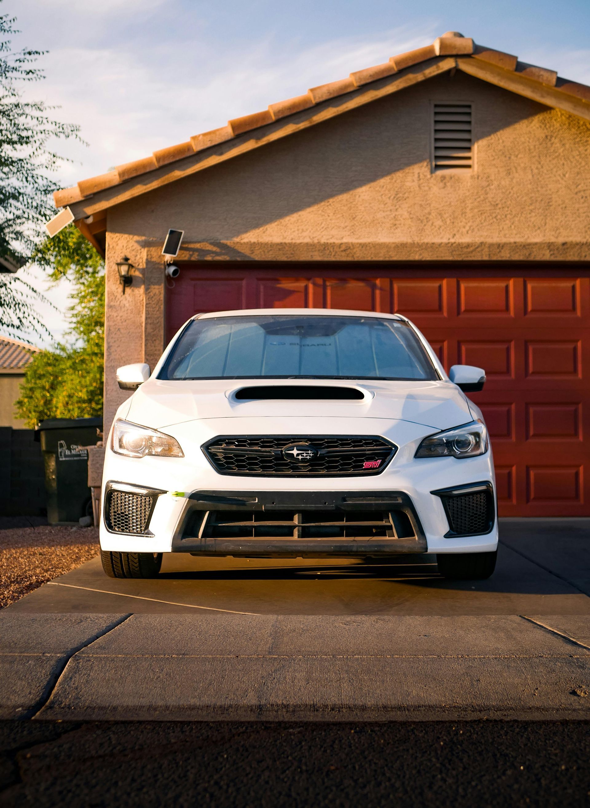 White Subaru WRX STI parked in front of a garage, facing the viewer.