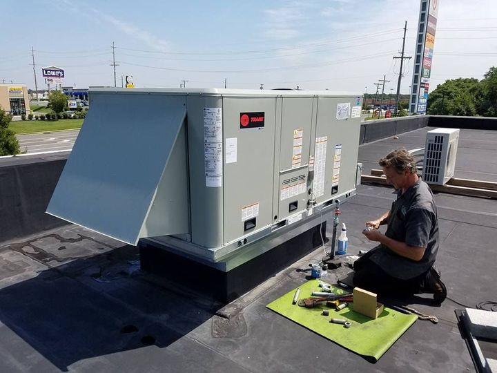 Climate Control Services technician kneels beside a rooftop HVAC unit, inspecting tools on a green mat