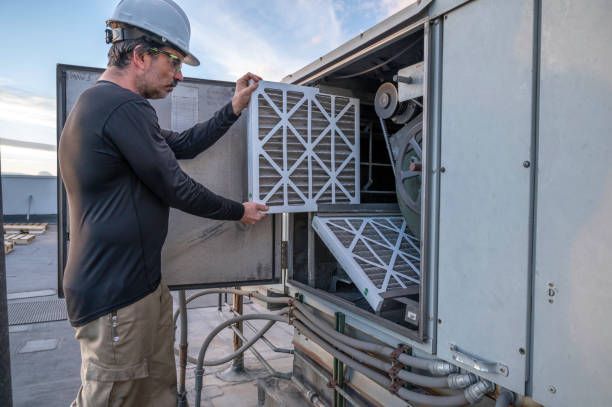 Technician replacing a rooftop HVAC filter unit on a building exterior