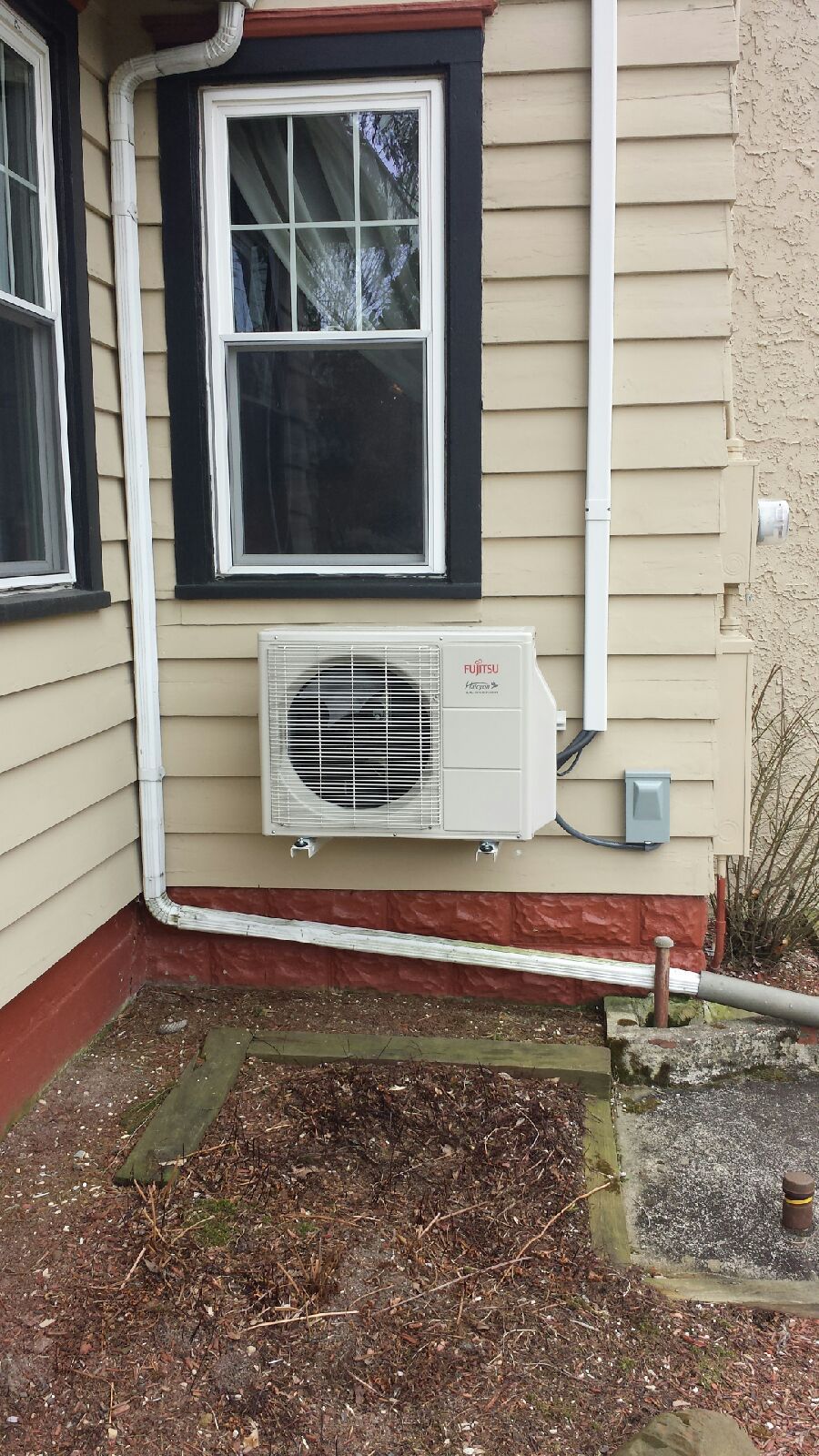 Outdoor Fujitsu wall-mounted air conditioner under a window on a beige house exterior