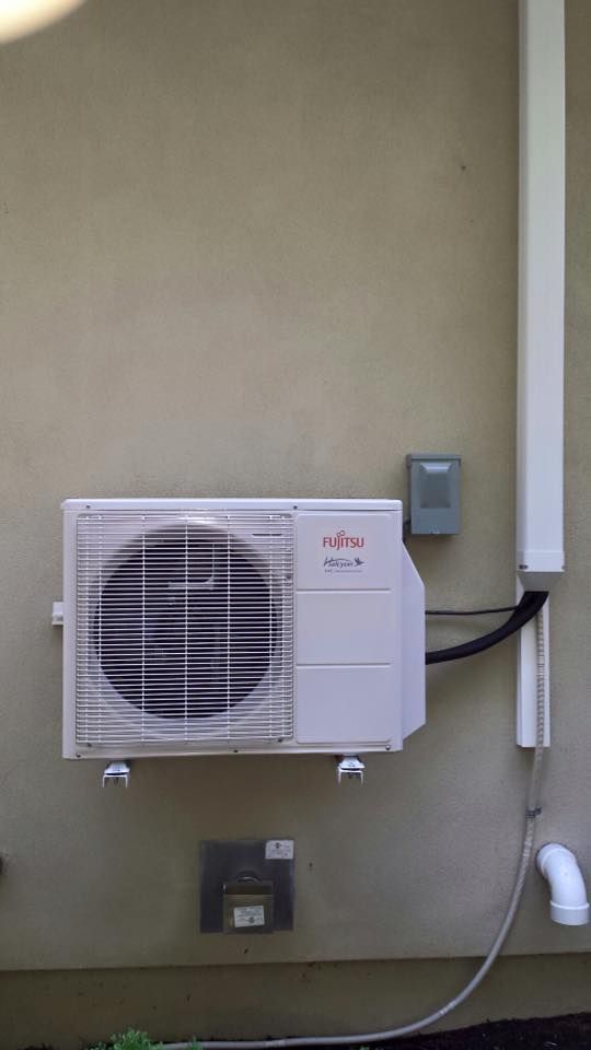 Wall-mounted Fujitsu air conditioner unit with visible outdoor fan and attached pipes on a beige wall