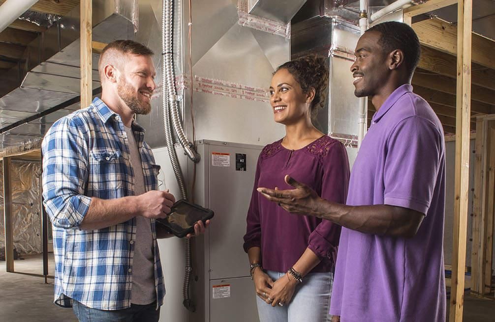 Three people talking beside HVAC ductwork in a basement utility room