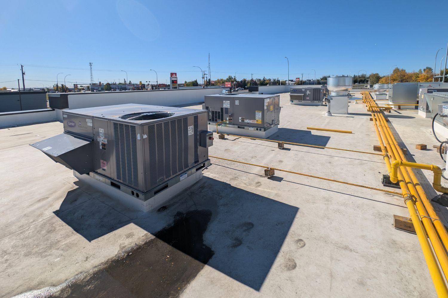Rooftop with HVAC units and yellow safety rails under a clear blue sky