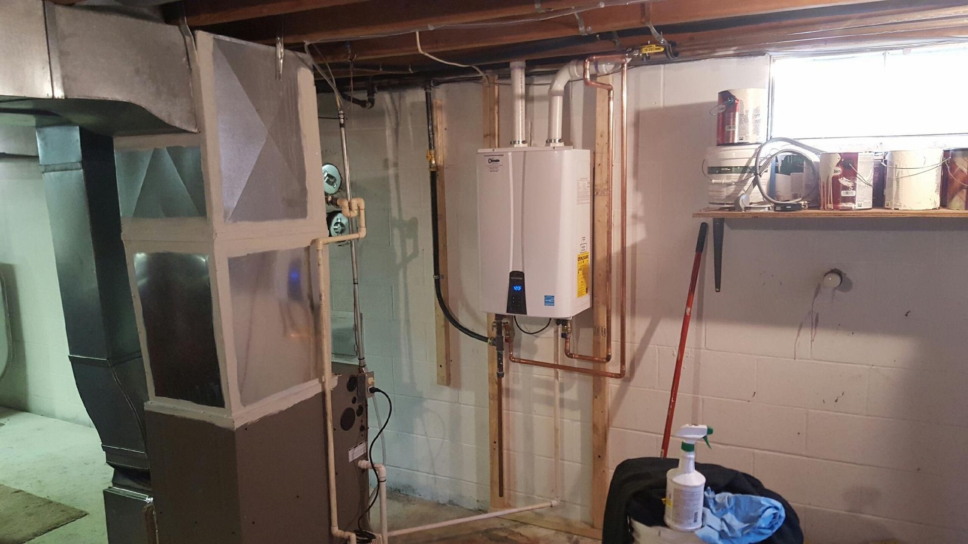 Basement utility room with tankless water heater, exposed pipes, shelving, and a small window