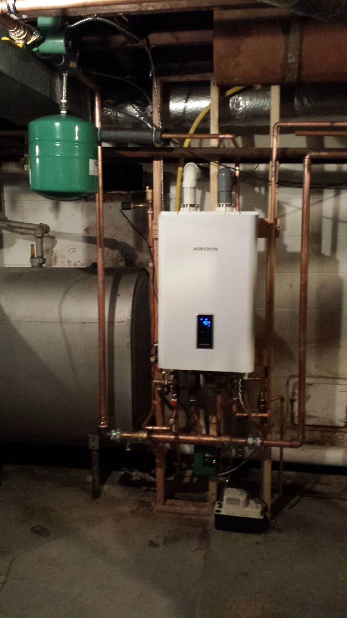 White wall-mounted tankless water heater unit and green tank in a basement utility room