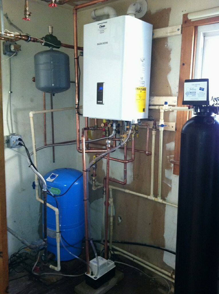 Boiler room with wall-mounted water heater, blue tank, pipes, and plumbing equipment against unfinished walls