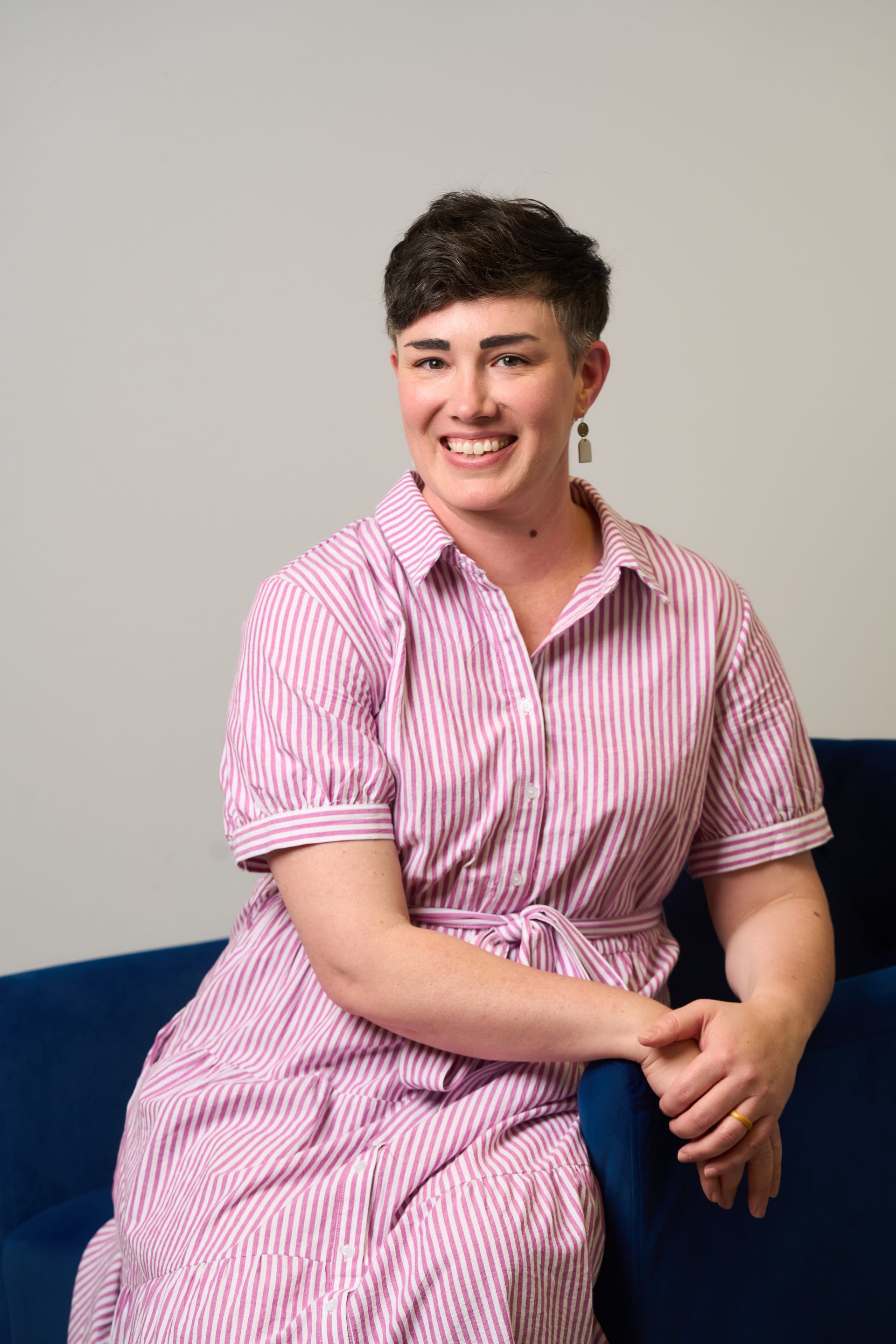 Person sitting on a blue couch, smiling in a pink striped shirt and purple pants.
