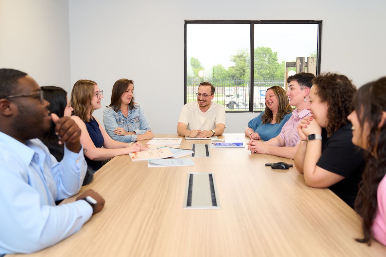 People seated around a conference table in a bright meeting room, talking and listening