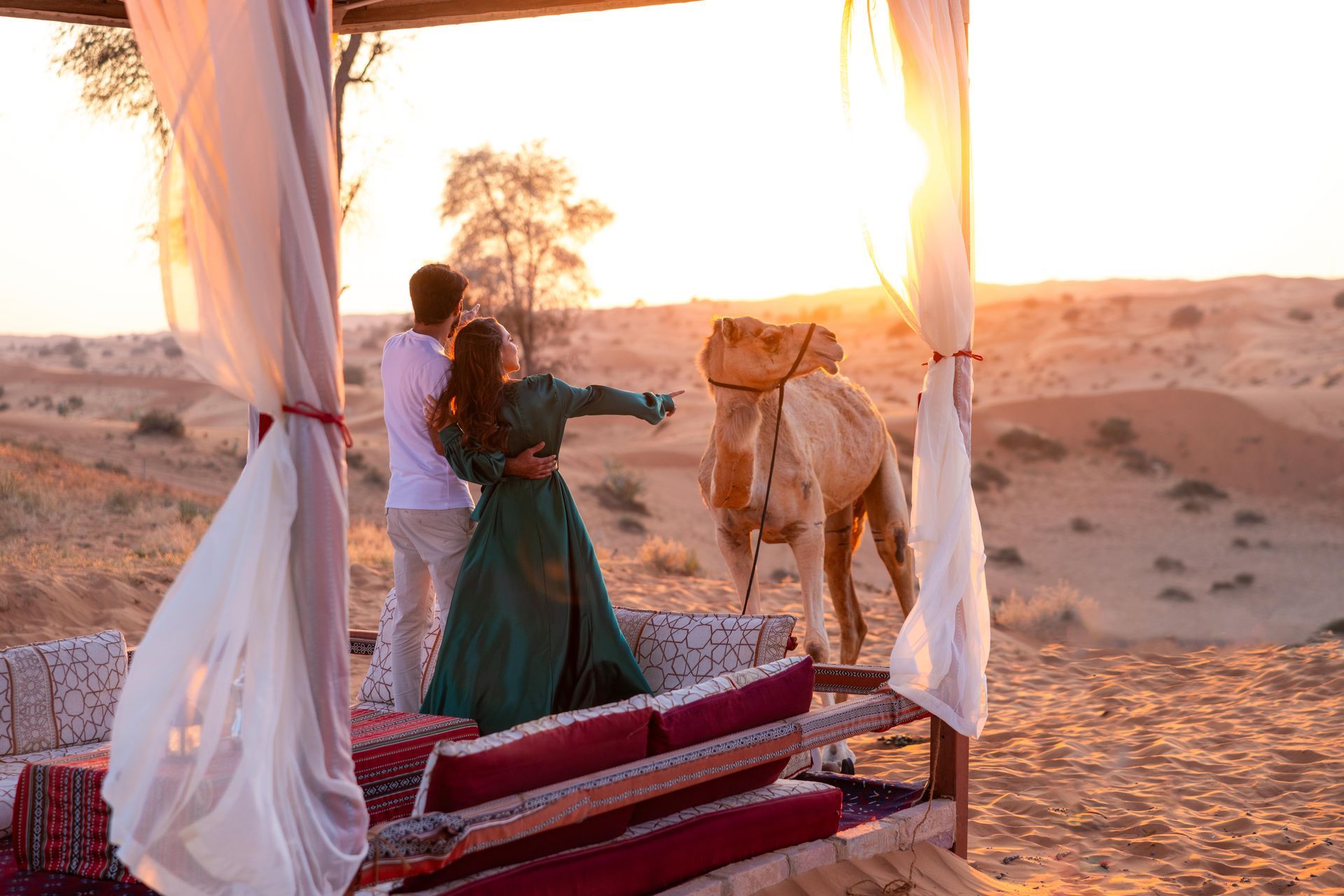A couple enjoying a scenic sunset at a desert camp with a camel