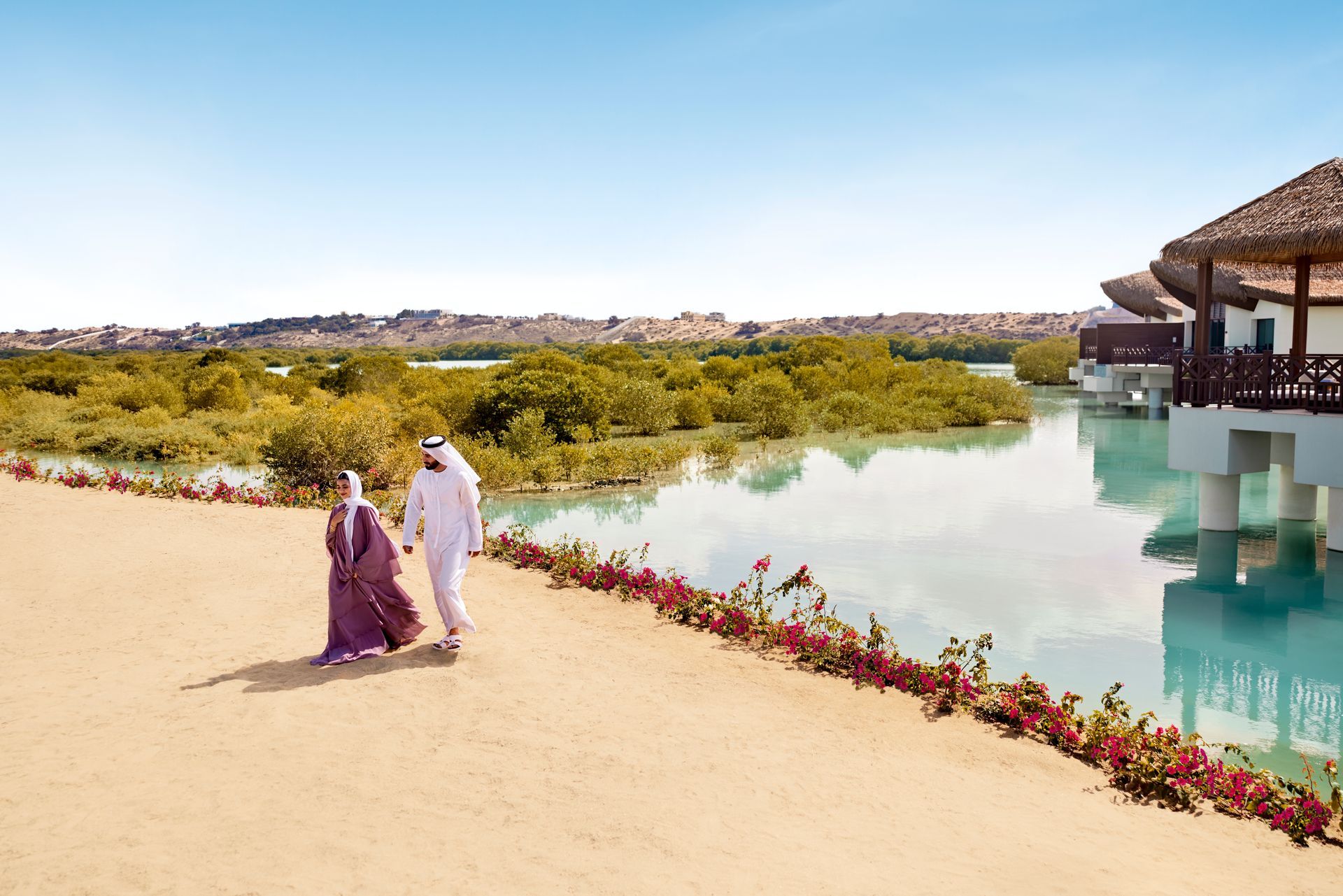 A couple walking at the Anantara Mina Ras Al Khaimah Resort, featuring overwater villas in a natural mangrove lagoon