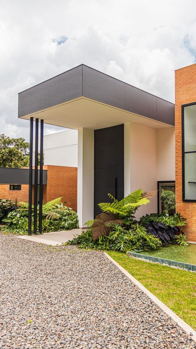 Entrada moderna a la casa con un toldo oscuro, camino de grava y un pequeño jardín paisajístico.