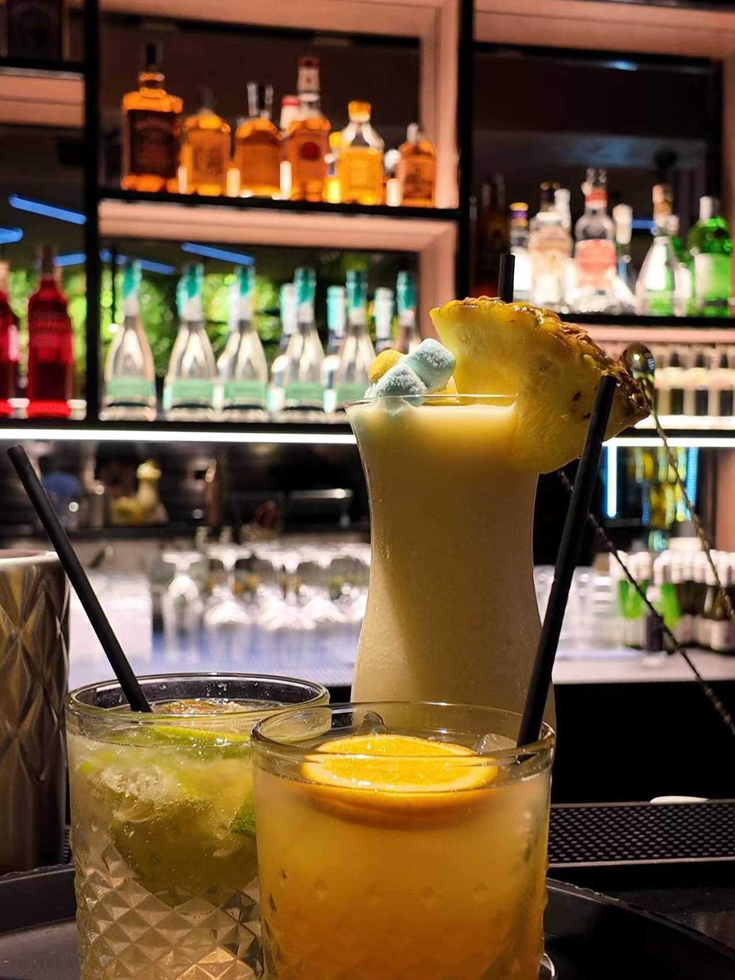 Cocktail giallo in un bicchiere con bordo di sale e uno spicchio di lime, su una superficie bianca, sfondo blu scuro.