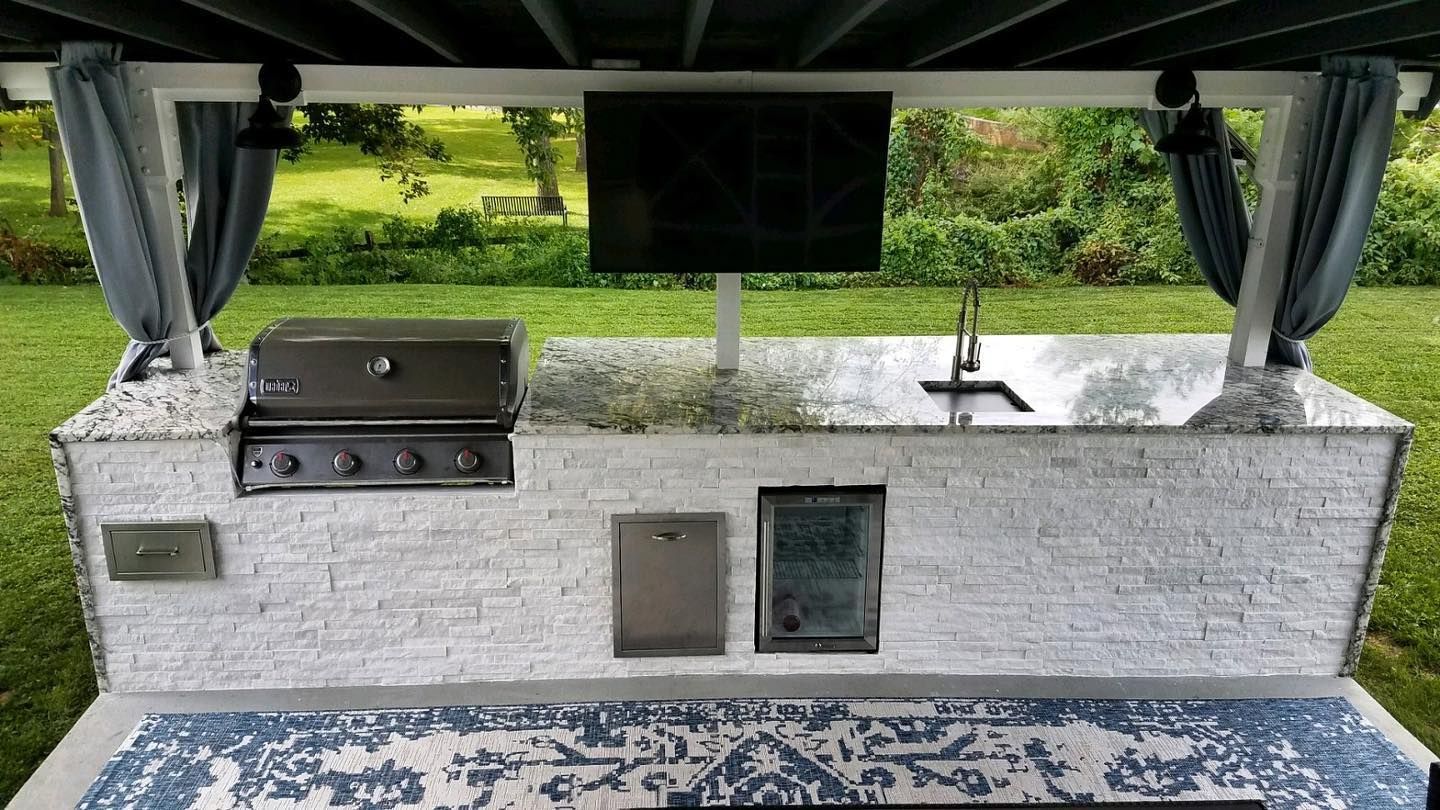 A large outdoor kitchen with a grill and a flat screen tv.