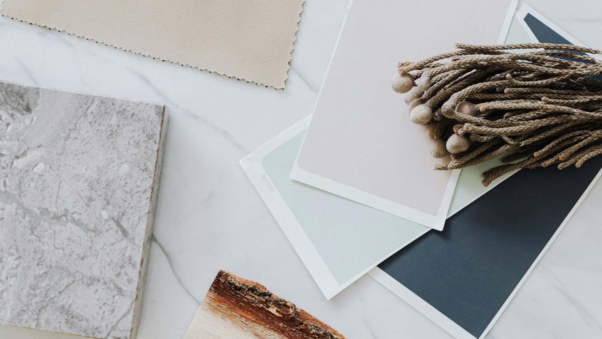 Color swatches and textures on marble: beige, pink, blue-gray, brown, and textured paper with a bundle of dried plants.