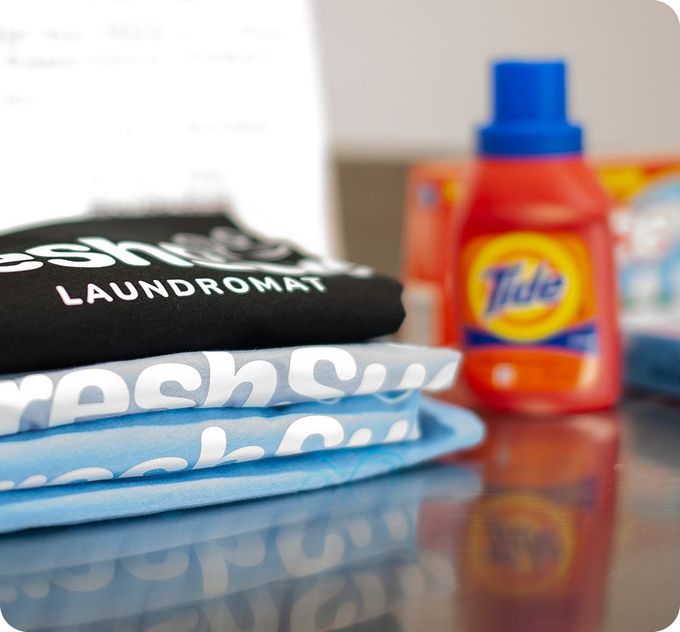 Stack of folded laundry, Tide detergent, and a laundromat sign. Fresh Suds Laundromat Memphis TN.
