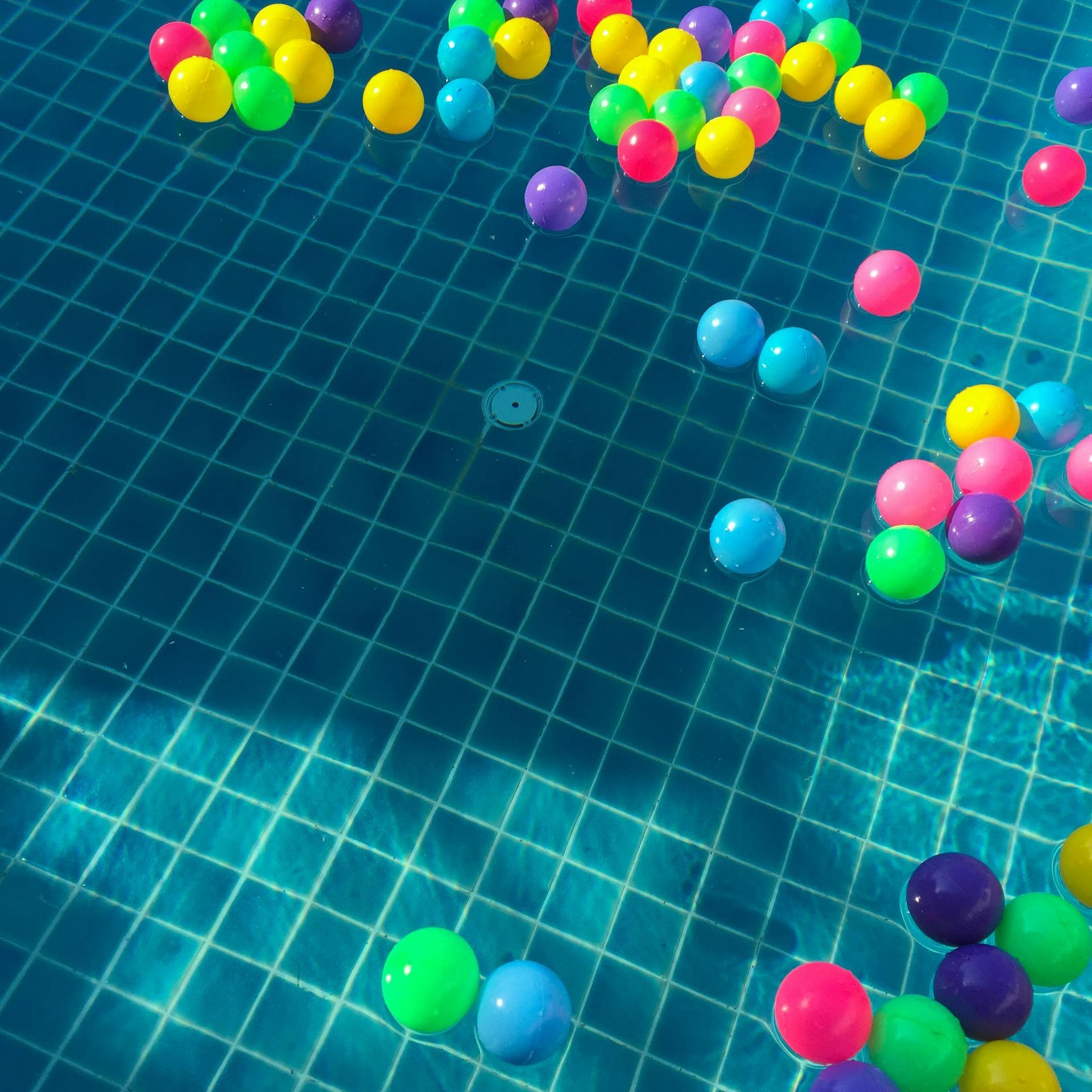 Bolas de plástico de colores flotando esparcidas sobre la superficie azul de una piscina.