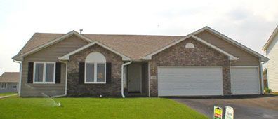 A single-story house with tan siding, brown roof, and a brick front, with green lawn in front.
