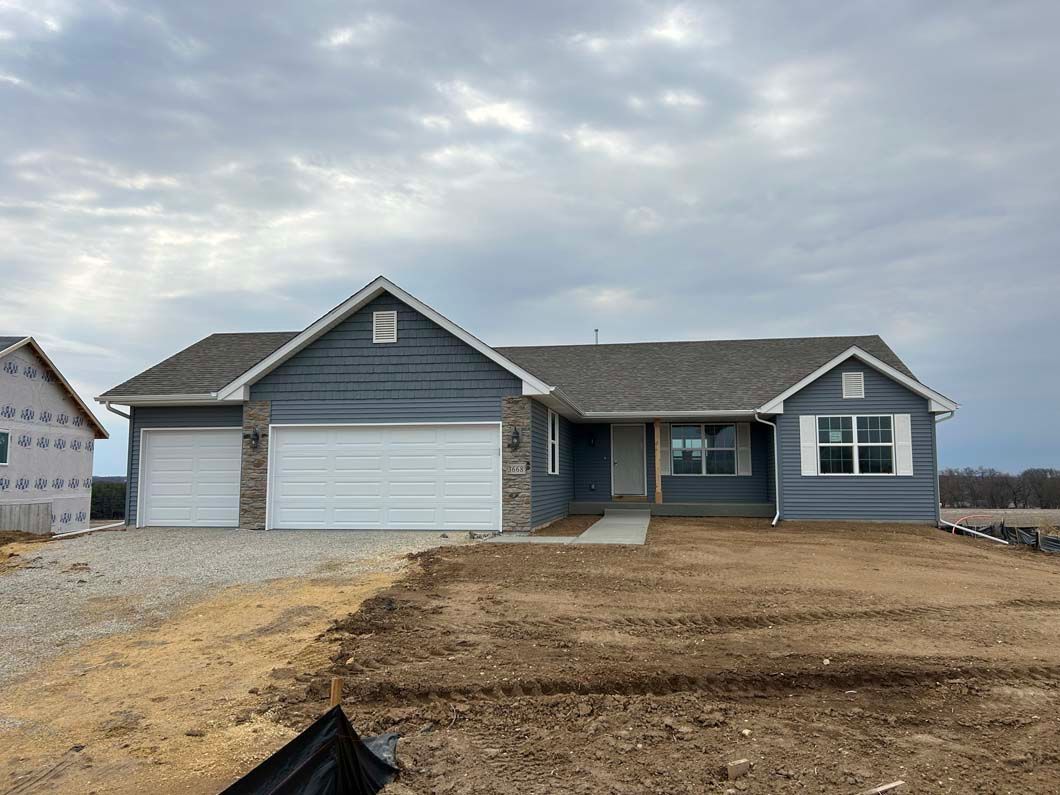 New construction ranch-style house with a gray exterior, stone accents, and a two-car garage.