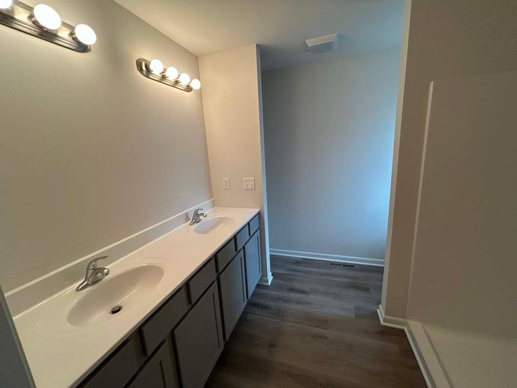 Bathroom with gray vanity, white countertop, and dark floor. Pathway leads to a shower area.