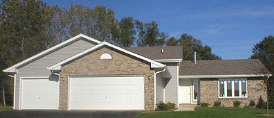 A single-story home with a gray roof, brick facade, two-car garage, and blue sky background.