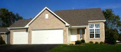 Brick house with two garage doors and a window, set on a green lawn under a blue sky.