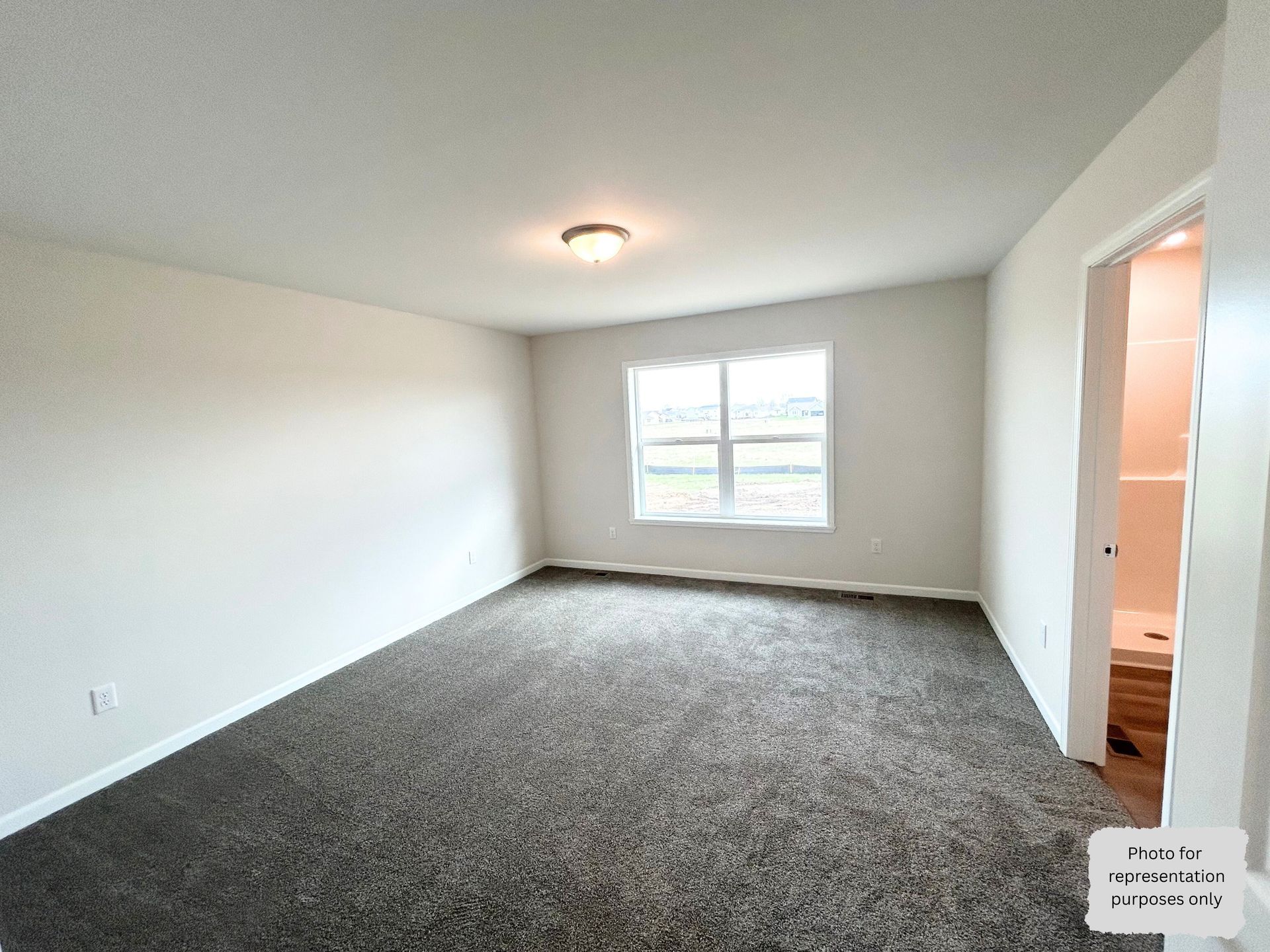 Empty bedroom with grey carpet, a window, and a door leading to a bathroom.