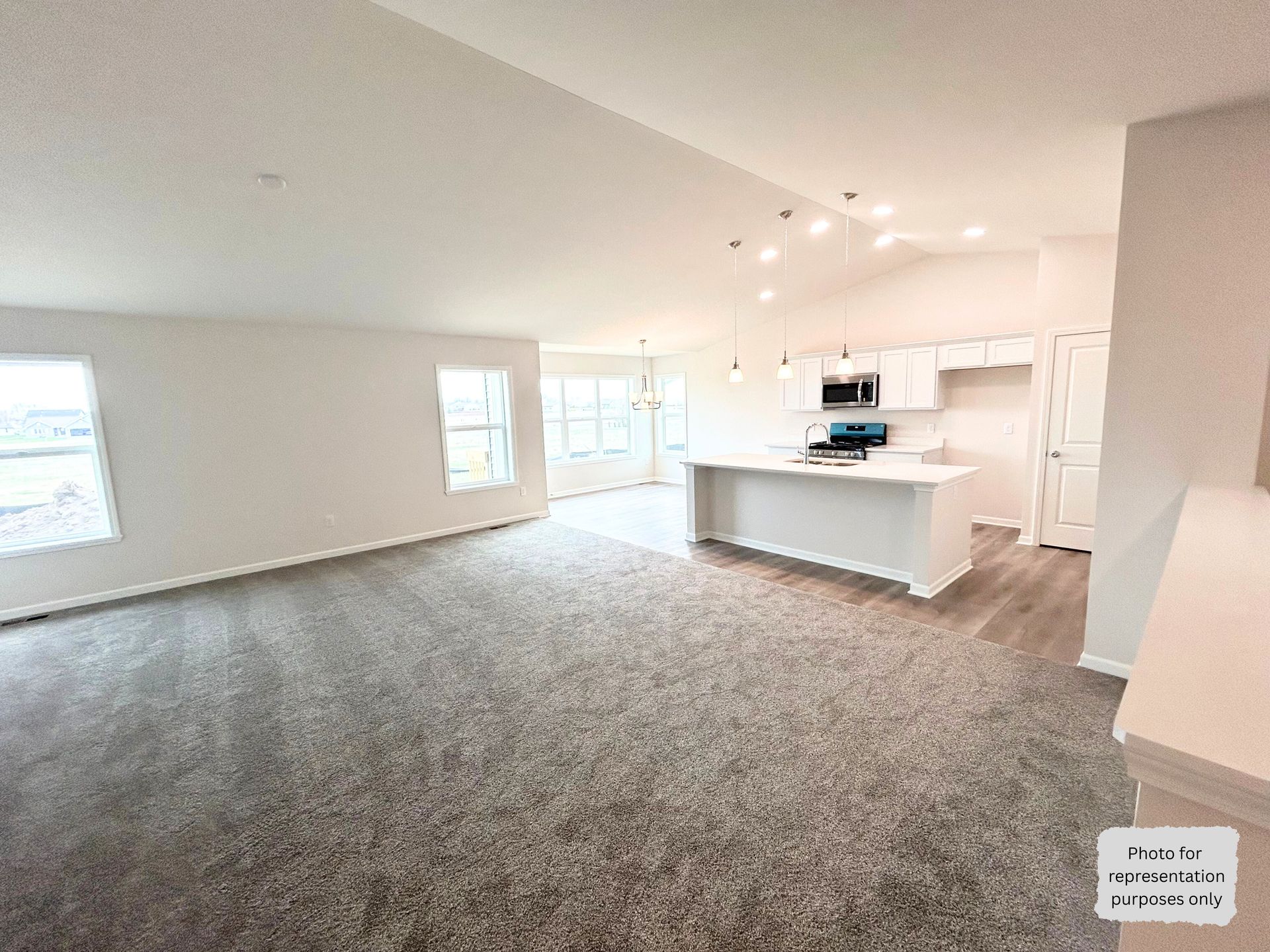 Open-concept living space with kitchen and living room. White walls and cabinets, grey carpet, and a kitchen island.