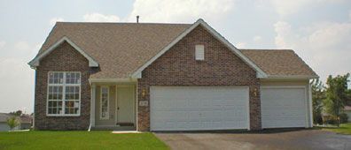 Brick house with a two-car garage and lush green lawn on a sunny day.