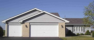 A two-car garage with a light-colored brick facade, a blue sky, and a house.