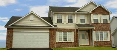 Two-story brick and beige house with a garage, white trim, and green lawn under a blue sky.