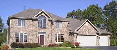 Brick house with a dark red door, two garage doors, and a blue sky.