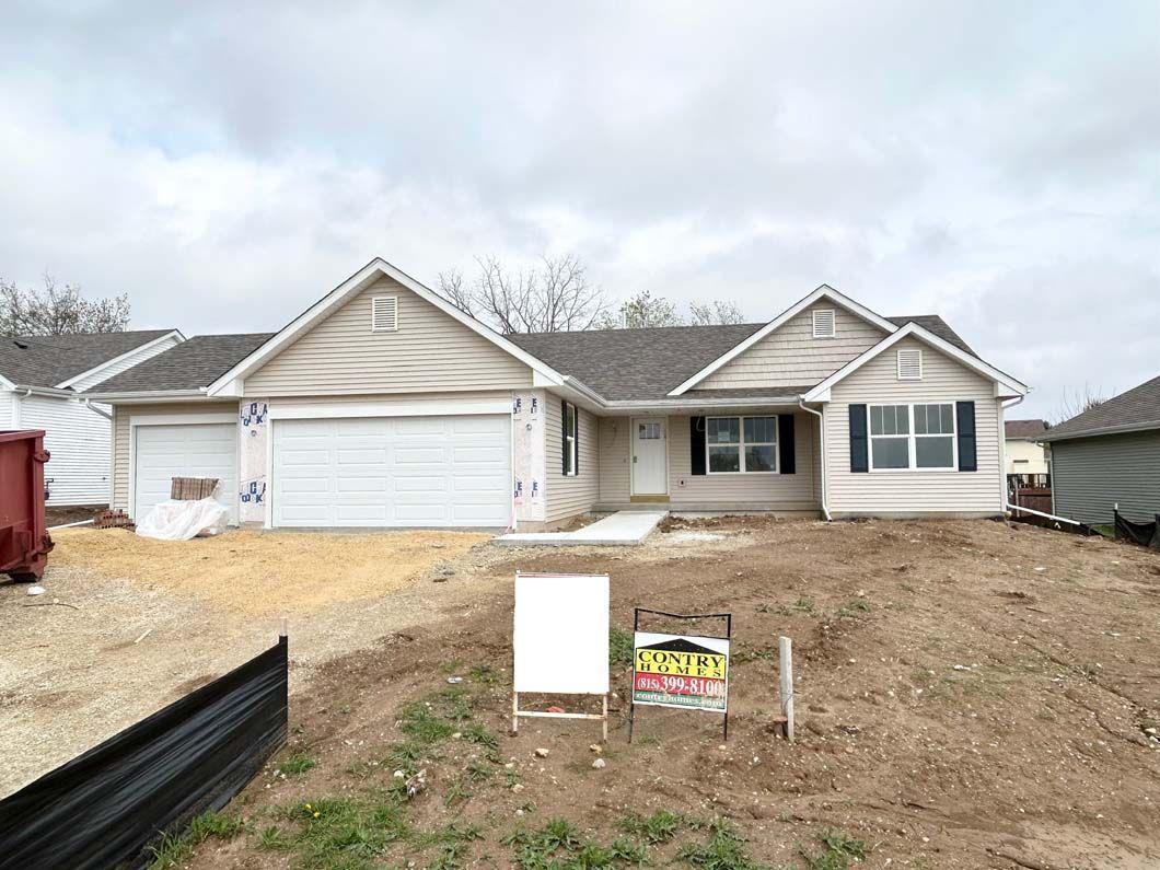 New construction house with beige siding, a two-car garage, and a blank sign in the yard.