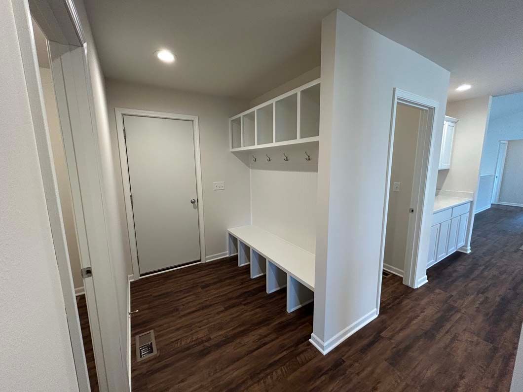 Hallway with a white mudroom bench and storage. Dark wood-look floors and white walls. Door on left and right.