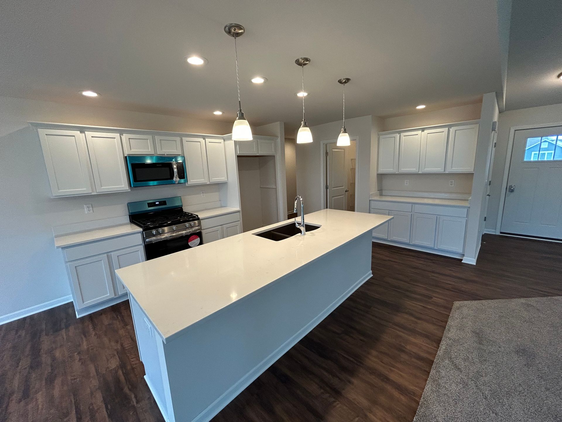 White kitchen with a long island, pendant lights, and dark wood floors.